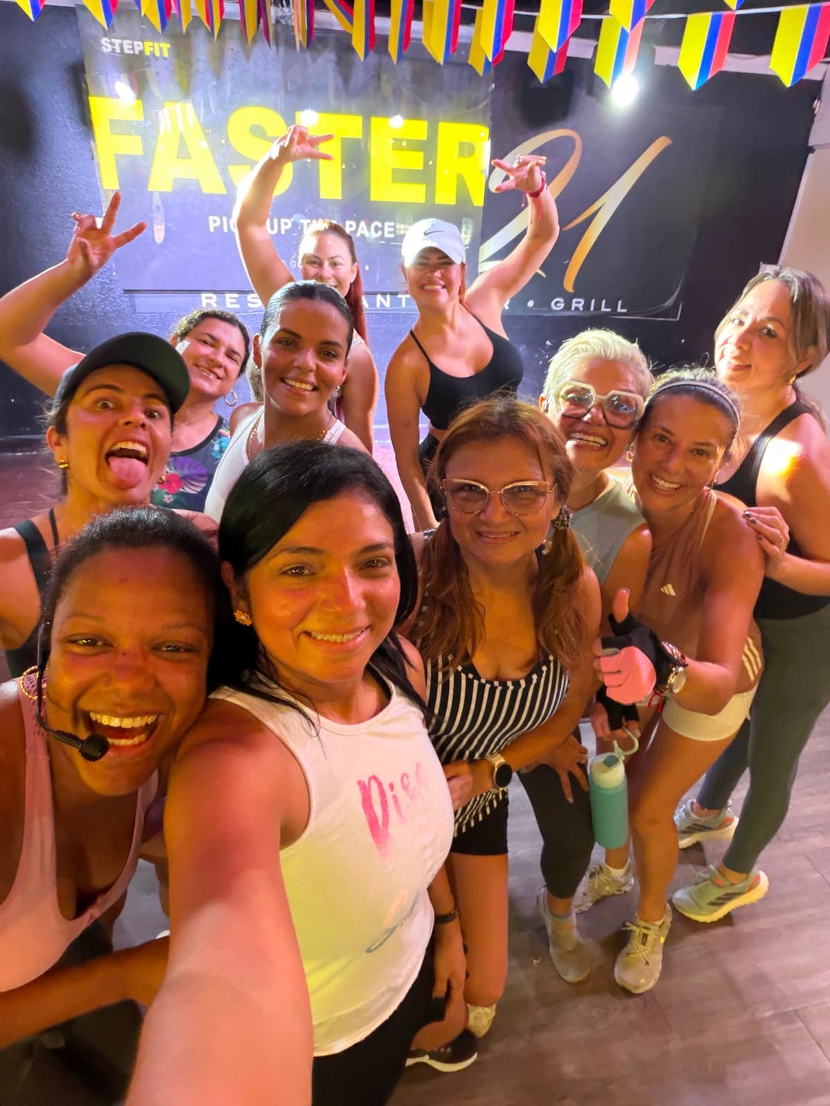 A group selfie held at arm's length after class, faces filling the frame, paper bunting overhead and FASTER, PICK UP THE PACE projected behind.