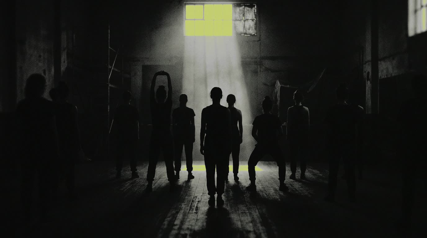 A dark room of backlit figures facing the front of a STEPFIT class, no faces visible